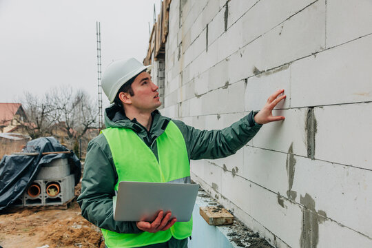Inspector with digital tablet examines aerated concrete wall at construction site