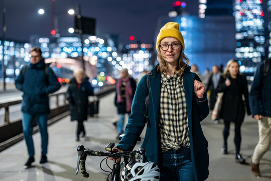 Urban commuter with bicycle in London at night wearing beanie