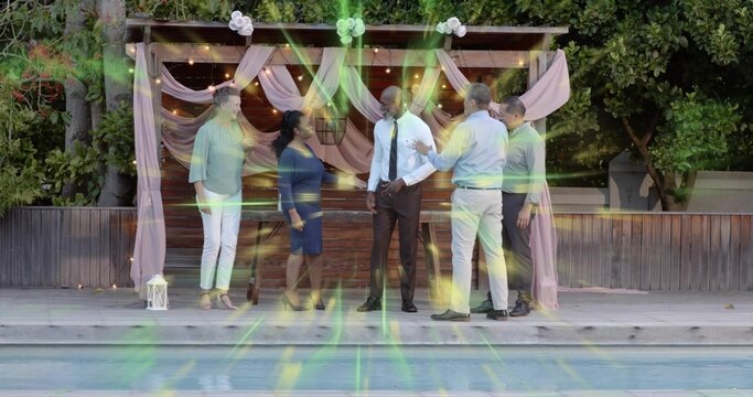 Standing six guests in smart outfits chatting on wooden deck near pool under pink pergola, lantern