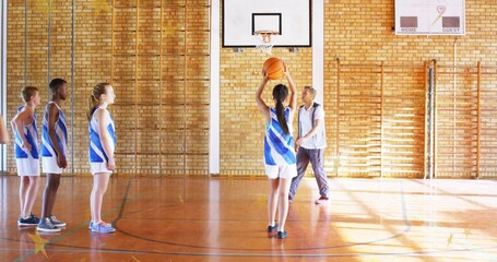 Obraz premium Holding teenage shooter raising basketball under hoop at gym, coach guiding teammates in jerseys