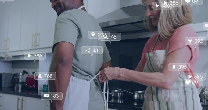 Woman approaching man, tying apron for cooking while social media icons multiplying around stove