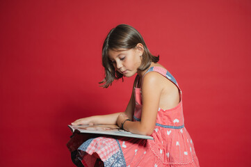 Young girl reading book studying against red background
