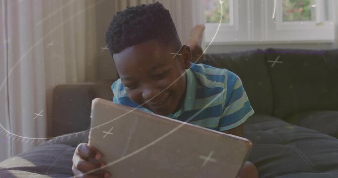 Boy tapping tablet on couch, causing animated swirls while sitting up for fun in education app