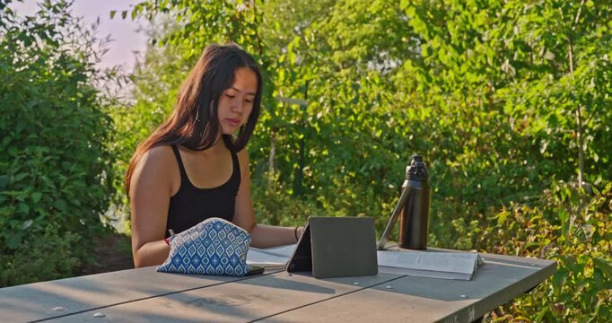 Ethnically ambiguous female student reviewing class notes in her notebook while outside.