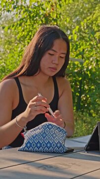 Smiling female student pulls pen out of a pencil pouch while reviewing her class notes in an outdoor setting.
