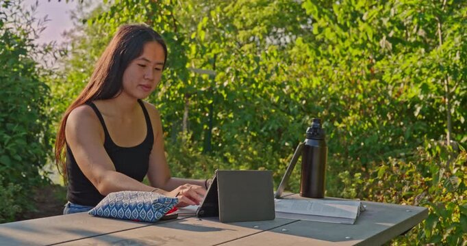Pacific Islander female student reviews class notes in an outdoor park setting.