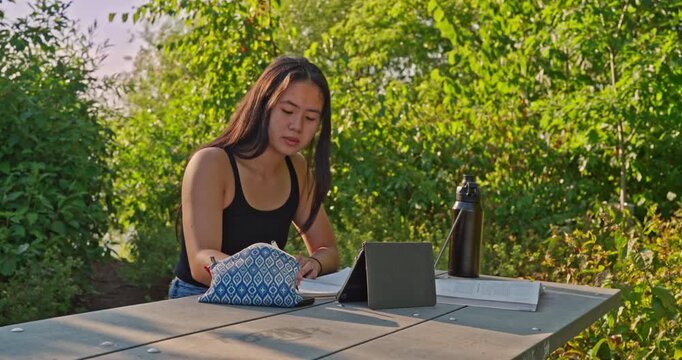 Ethnically ambiguous female outdoor studying for school in an outdoor park setting on a sunny afternoon.