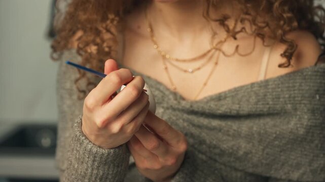 Curly-haired Woman Painting Colorful Tiny Dots On White Egg - Easter Egg Decorating. closeup shot