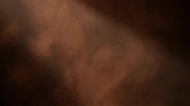Fine cocoa powder swirling through a dramatic shaft of light against a dark background