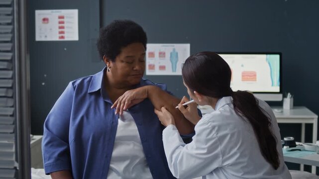 Female doctor performing skin marking on Black female patient arm prior to diagnostic examination in modern clinic, eyelevel medium shot