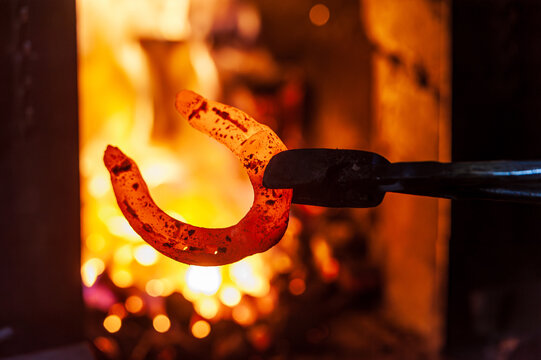 Close-up view of a glowing hot horseshoe held with tongs inside a blacksmith forge. Traditional metal heating process symbolizing craftsmanship, heat and rural heritage.
