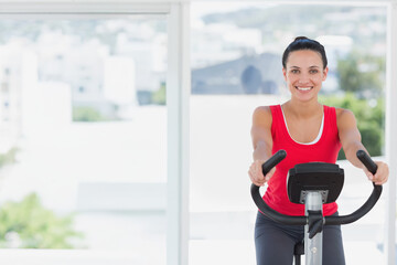 Adult female cycling exercise bike with console and handlebars wearing red top at home, copy space