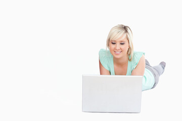 Naklejka premium Adult woman reclining on white backdrop wearing mint top and hoops using silver laptop, copy space