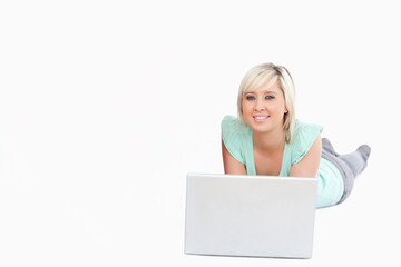 Woman lying propping on elbows on white backdrop using silver laptop wearing mint top, copy space © wavebreak3