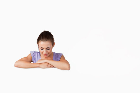 Woman leaning forward, arms on white ledge in studio in lilac top, looking down, copy space