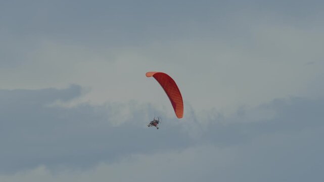A red paraglider small airplane is flying above the city with a tourist passenger.