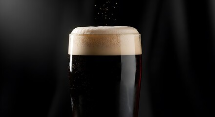 A glass of stout beer with a dense, creamy head, dark background, studio light highlighting the contrast.