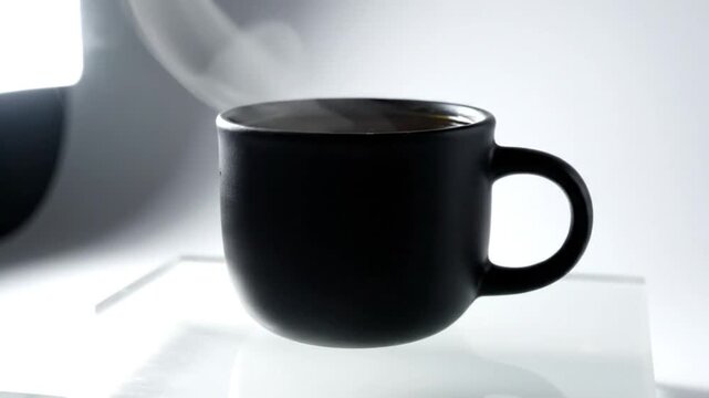 Black coffee mug with steam rising against a bright white background, slow motion capture
