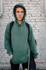 Young man in hoodie holding skateboard outdoors