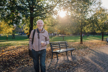 Senior man enjoying autumn park walk with coffee