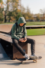 Teenager sitting using phone in skate park