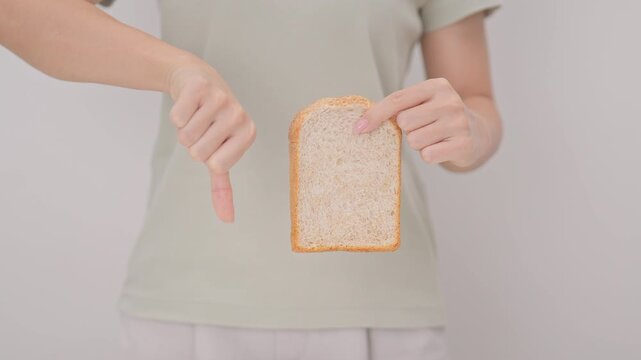 Unhappy woman showing thumbs down gesture and refusing to eat bread. concept of gluten intolerance, gluten sensitivity, carb loading concerns, or a disliking for unhealthy dietary habits
