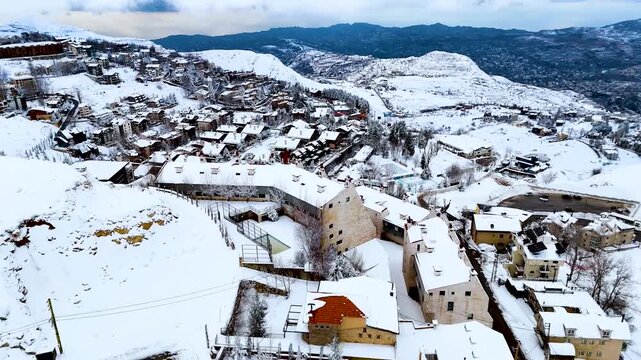 Drone shot of Kfardebian village blanketed in snow with mountain backdrop. Winter tourism destination featuring chalets, hotels and alpine landscape in Lebanon.