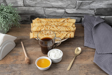Stack of rolled pancakes with honey, yogurt, and coffee on a table with stone wall background