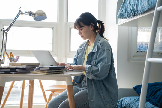Student asian woman sitting on bed in dorm room college student&nbsp;Work or homework on laptop in university dormitory