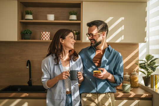 Couple enjoying morning coffee and smart phone together in kitchen