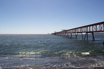 Obraz premium Long Red Industrial Pier Structure Extending Over the Ocean