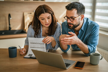 Couple discussing budget and finances at home kitchen desk © Miljan Živković