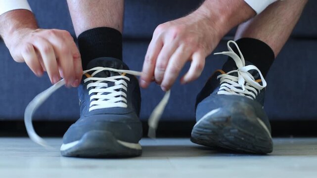 Close up of hands tying white laces on worn navy sneakers, capturing a grounded, everyday ritual of preparation, comfort, and quiet readiness.
