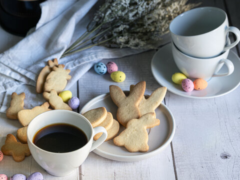 Easter breakfast, coffee and Easter-shaped cookies on a table with flowers and colorful eggs