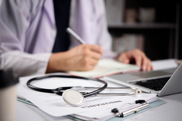 Naklejka na ściany i meble doctor hands writing on medical document with stethoscope and health insurance claim form on desk. Concept of healthcare coverage, life insurance policy and medical protection.