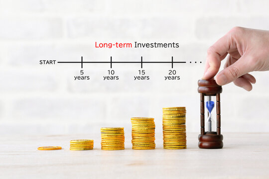 積み上げられた硬貨と砂時計を置く人物の手―長期投資イメージ