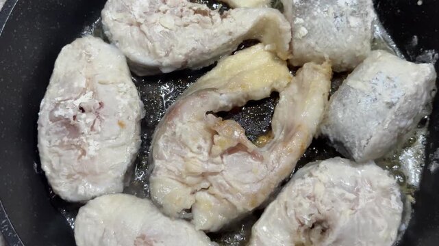 Raw fish steaks dredged in flour beginning to cook in hot oil. Ideal for cooking tutorials, recipe videos, and seafood restaurant promotional content
