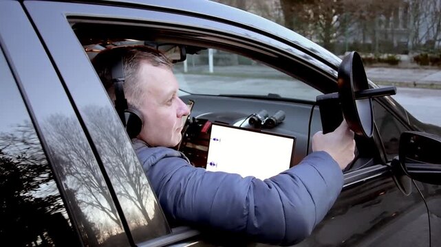 A man wearing headphones performs covert surveillance and records conversations using a directional microphone from a vehicle.