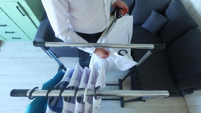A man hangs freshly pressed white shirts on a drying rack, highlighting routine care, order, and the quiet dignity of domestic responsibility.
