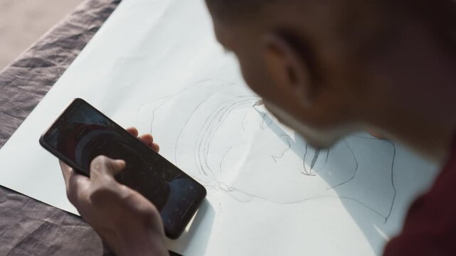 Artist sketches diligently. Illustrator creating detailed smartphone drawing. Skilled black illustrator carefully sketches phone reference along guide with precise focus and intent