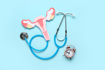 Stethoscope with paper uterus and alarm clock on blue background