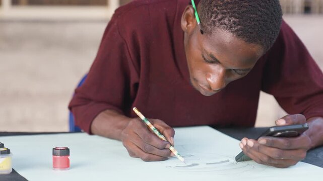 Man sketching with phone as reference. Individual painting detailed picture using mobile device outdoors. Male artist meticulously capturing portrait while referencing phone in natural sunlight