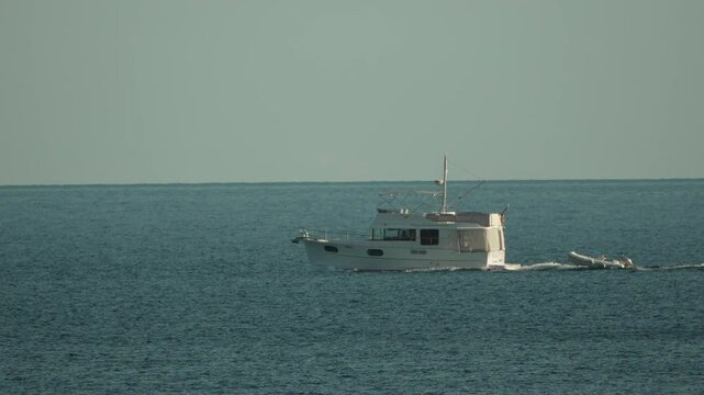 Boat, yacht, ocean: White motor yacht navigates calm blue ocean with dinghy