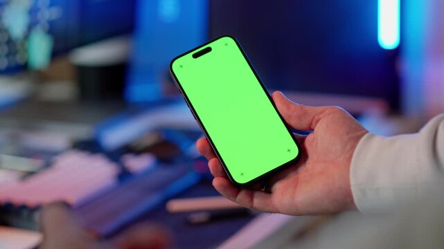 Smartphone green screen mockup hand closeup corner markers. Modern mobile device held palm shallow depth background home office desk blurred bokeh lighting chroma key display tracking markers
