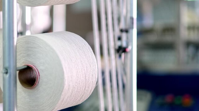 Professional industrial footage reflecting textile manufacturing process and infrastructure. Thread spools aligned on racks inside a textile factory production area.