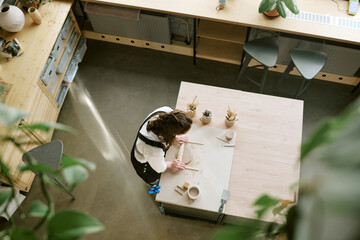 Caucasian young adult woman sculpting clay on worktable, shaping pottery with hands, surrounded by...