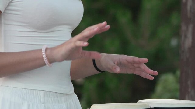 Woman playing drums, hands performing rhythmic beat on bongos outdoors