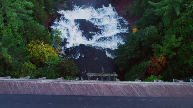 Drone shot of picturesque bridge spanning a gap with river and waterfall far below.
