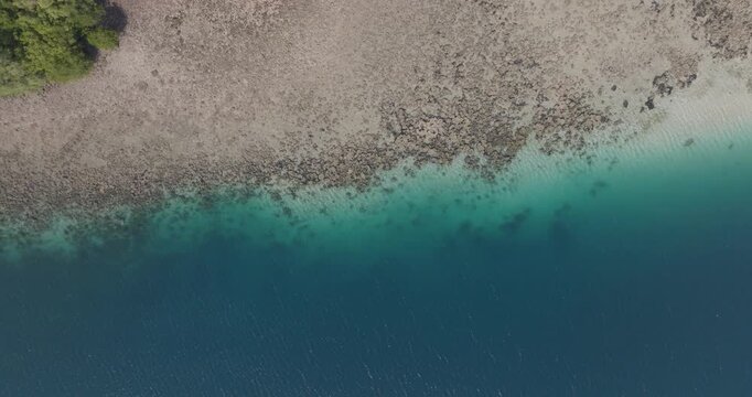 Top-down drone view of coral reef meeting deep blue ocean in West Bali National Park, Indonesia. Turquoise shallows, exposed reef and clear tropical water forming natural coastal patterns