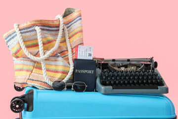 Suitcase with vintage typewriter and beach accessories on pink background, closeup